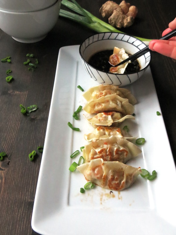 A plate full of homemade gyoza and one being dipped in the dipping sauce
