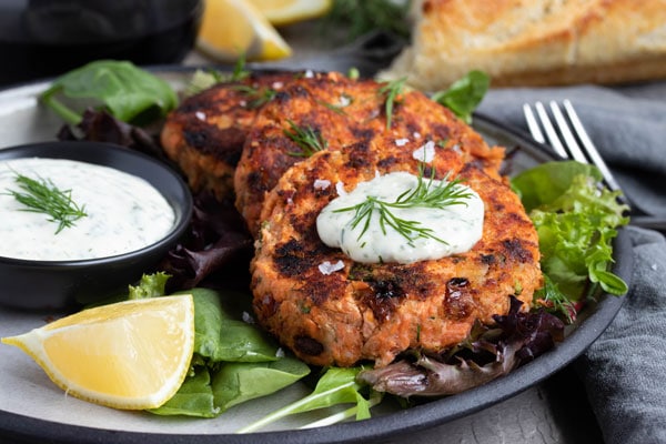 a horizontal picture of salmon cakes on a plate on a bed of spinach