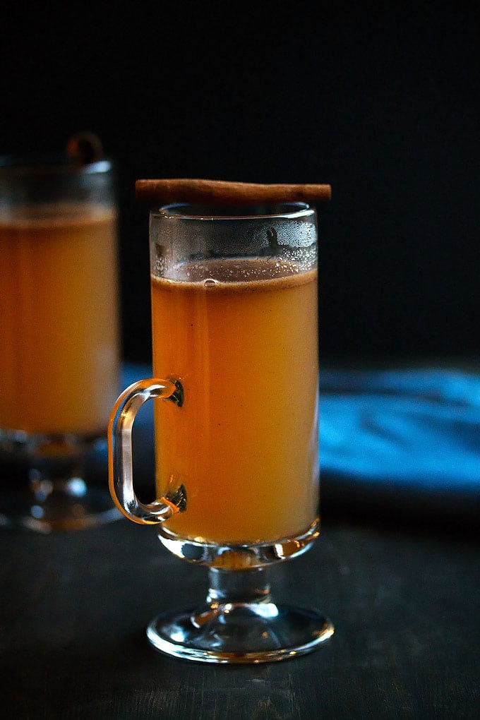 a mug of apple cider hot buttered rum with a stick of cinnamon on top