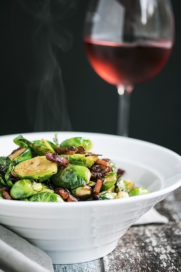 a bowl of pan fried brussel sprouts and a glass of wine