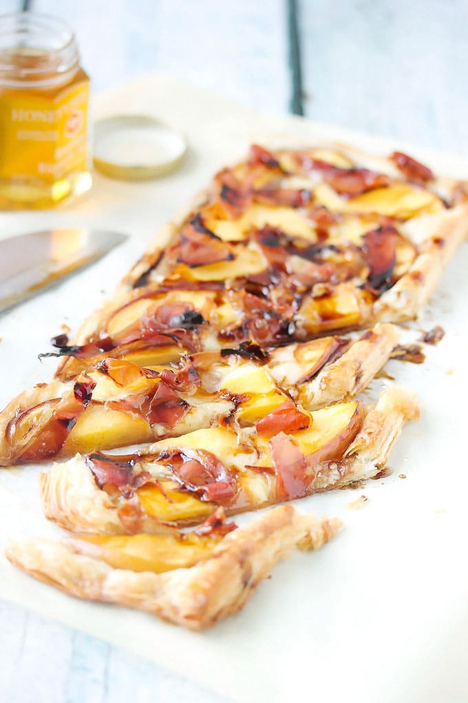 a peach and prosciutto tart that has been cut into a few slices and ready to eat. 