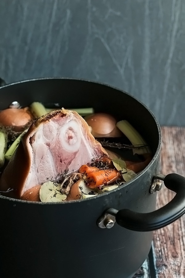 a pork shoulder in a pot with water and vegetables ready to cook