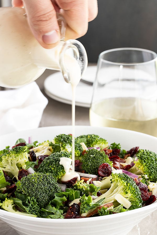 pouring the dressing on top of a bowl of broccoli salad