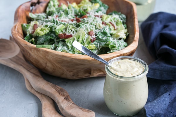 a bowl of caesar salad with a jar of homemade caesar salad dressing in front of it