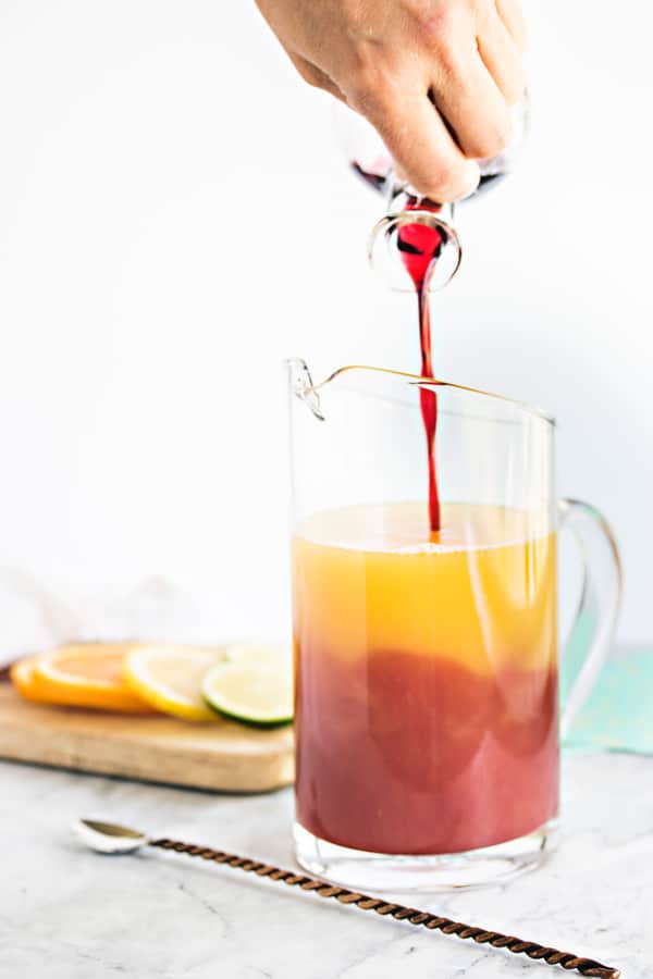 pouring the hibiscus syrup into a pitcher of juice