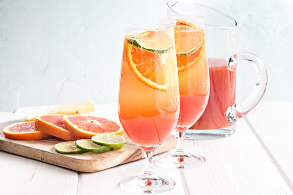 two glasses of rum punch with a pitcher and some slices of orange and lime