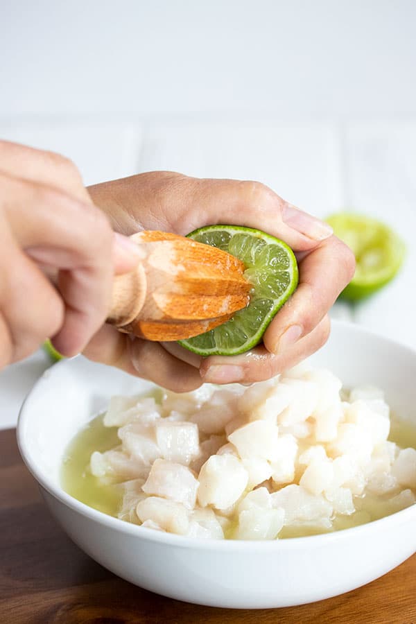 squeezing limes into a bowl of halibut ceviche