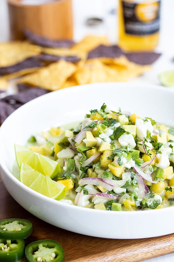 a bowl of halibut ceviche mixed with pineapple, red onion, and cilantro with chips in the background