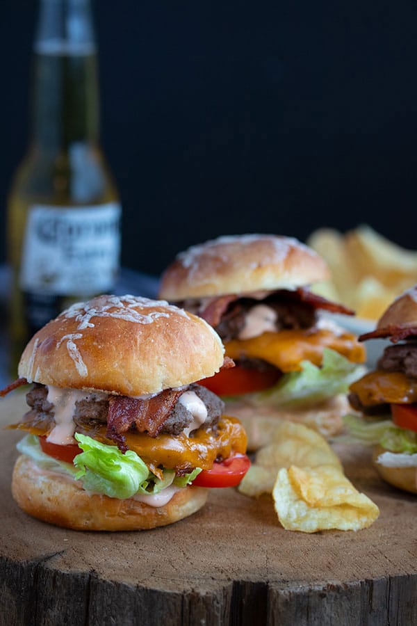 three sliders on a wood tray with some potato chips