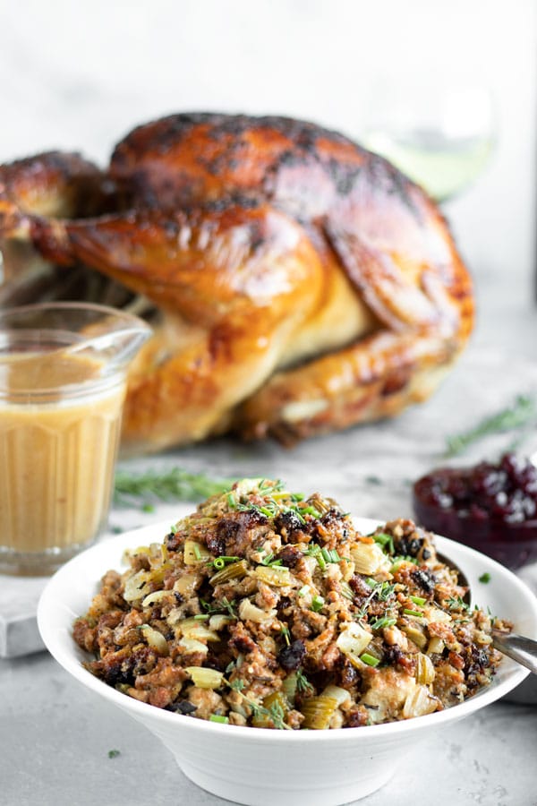 a bowl of turkey stuffing on the table with a turkey, cranberries and gravy