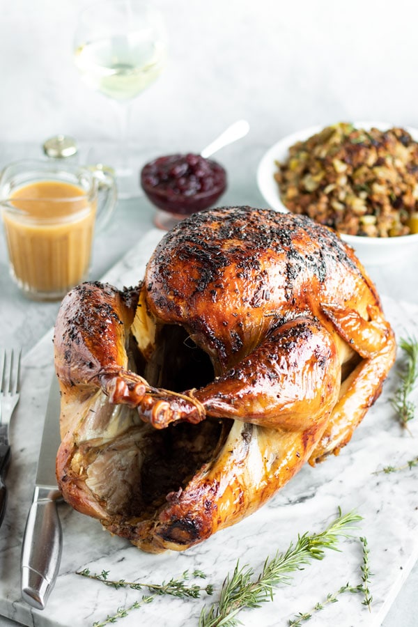 a brined turkey on a table with stuffing, gravy and cranberry sauce