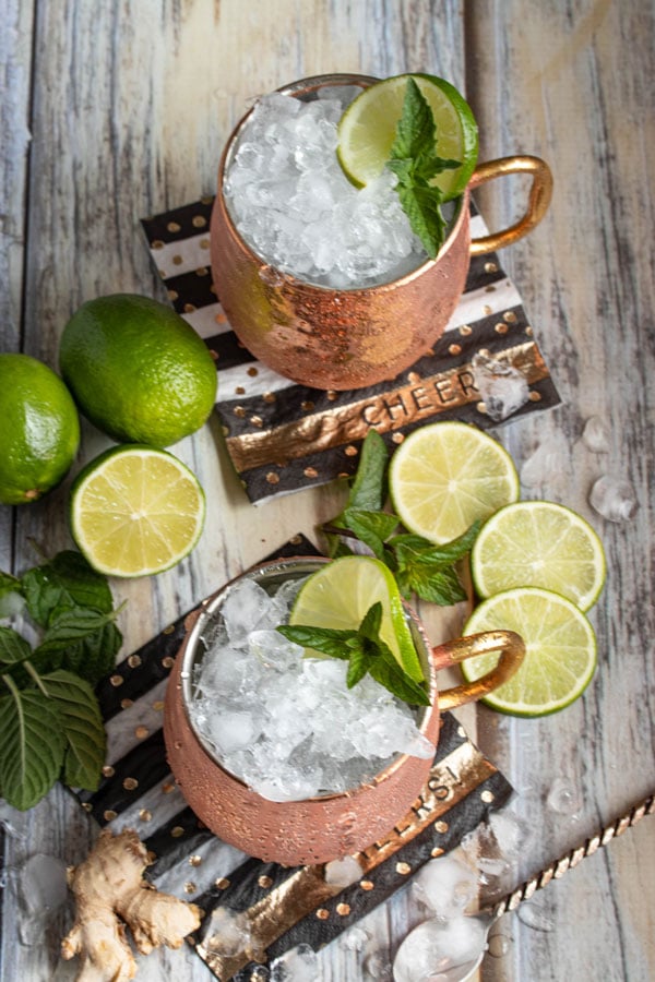 looking down on two moscow mule cocktails in copper mugs with lime wedges
