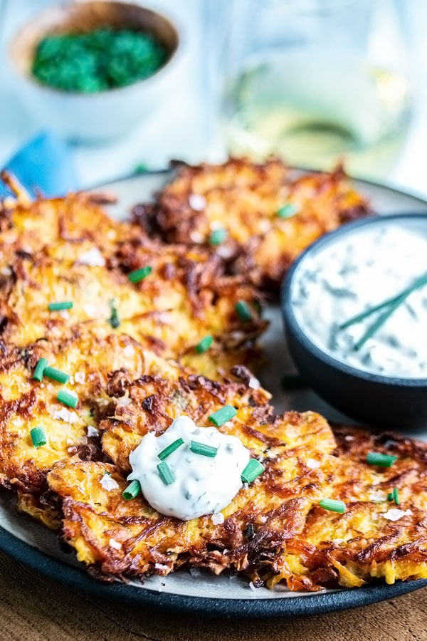 a dollop of sour cream sauce on one zucchini fritter out of a bunch on a plate