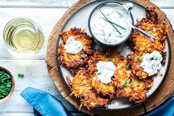 top down view of zucchini fritters on a plate with three of them dolloped with herbed sour cream sauce