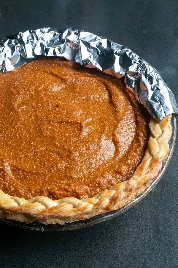 a blind baked pie crust with the unbaked pumpkin pie filling in it.  Part of the crust is covered with tin foil. 