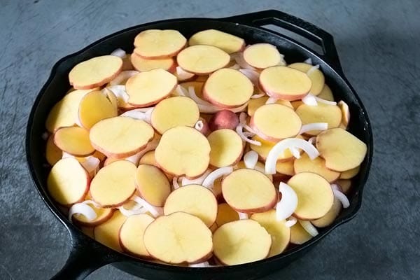 potatoes layered with onions in a cast iron skillet
