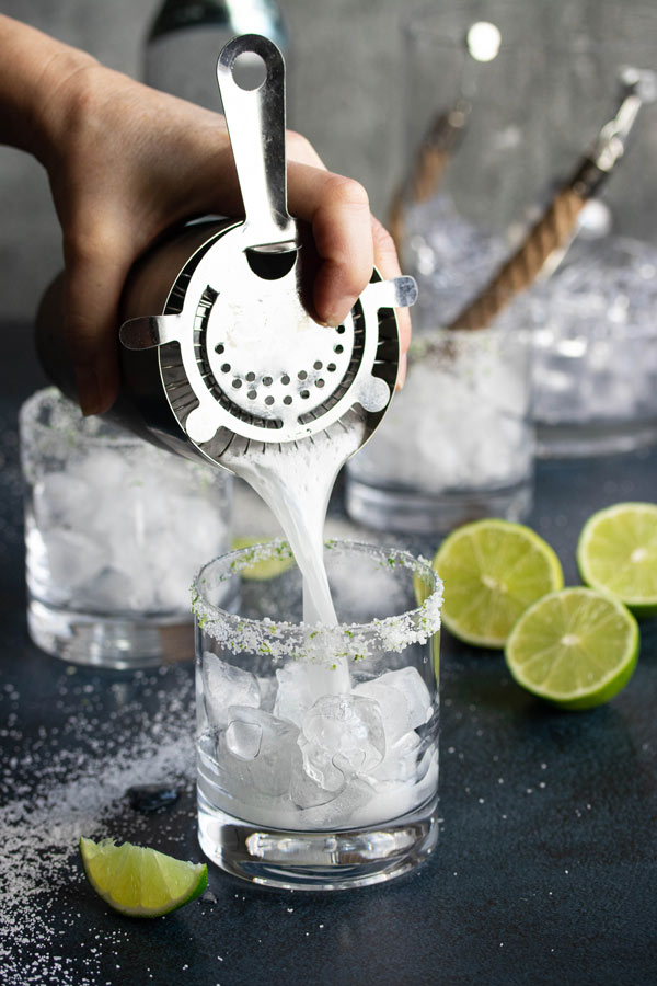 pouring a shaken margarita into a glass filled with ice