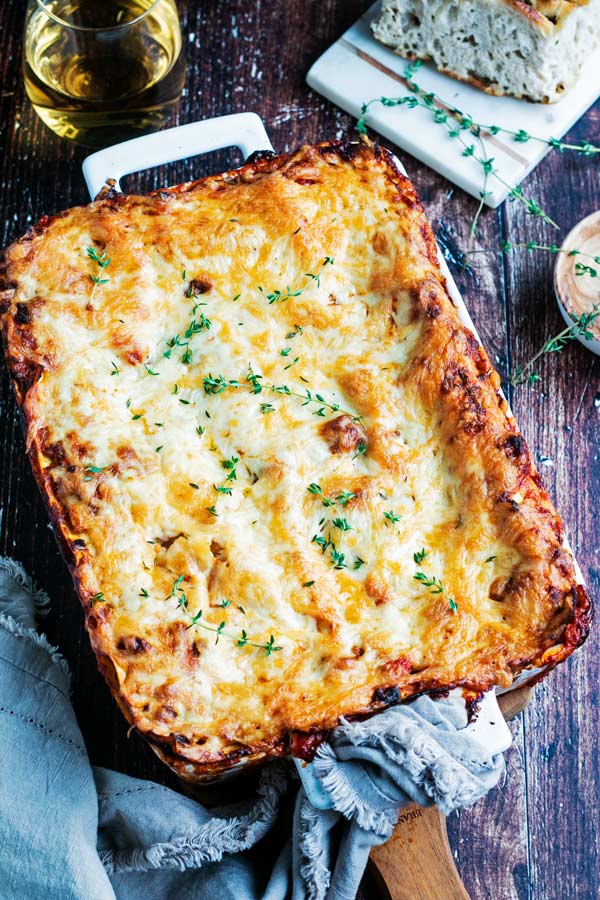 a freshly baked lasagna from the oven served with a glass of white wine and some bread
