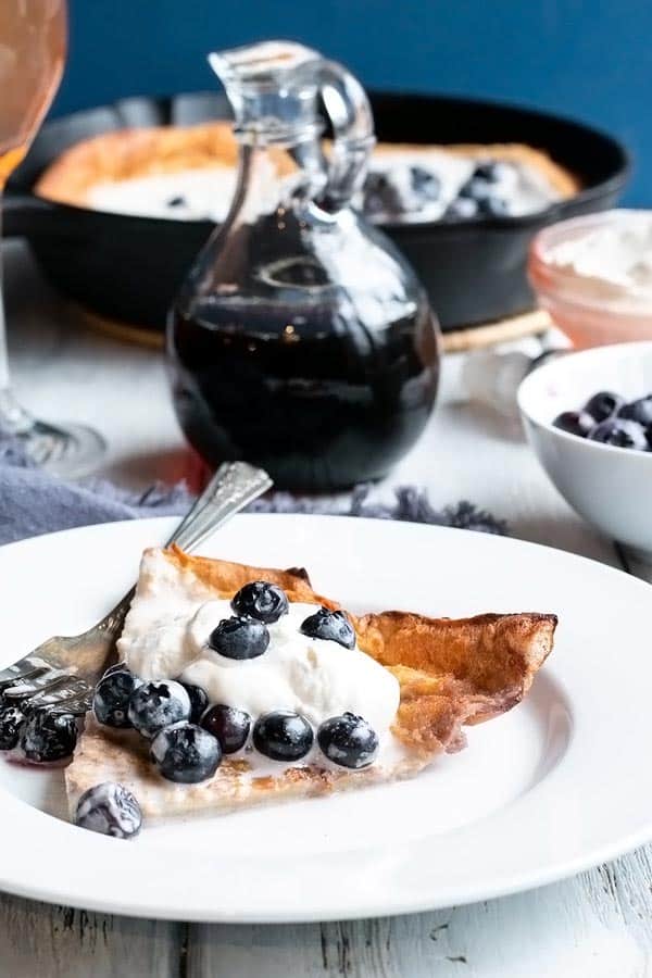 slice of dutch baby pancake on a plate with blueberries and whipped cream