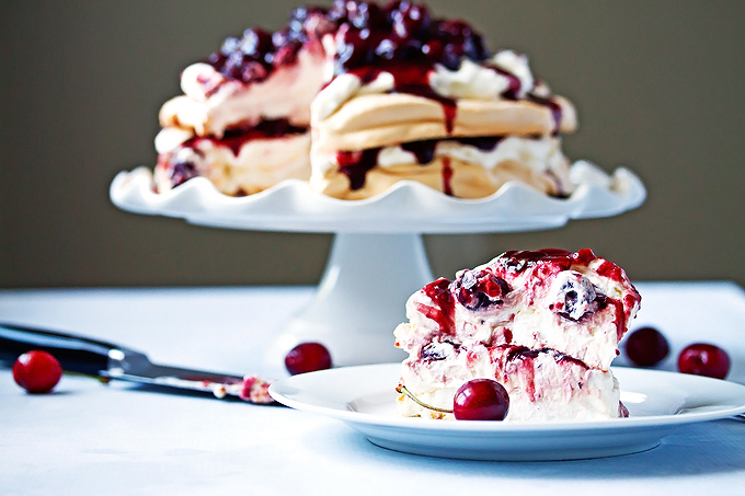 A piece of this pavlova recipe on a plate with the main dessert in the back ground