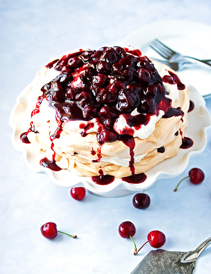 a beauty pavlova recipe on a cake stand with cherry compote dripping over the sides