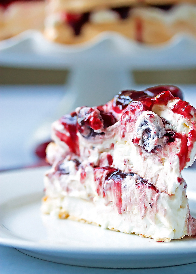A slice of pavlova on a plate with whipped cream and cherry compote on top