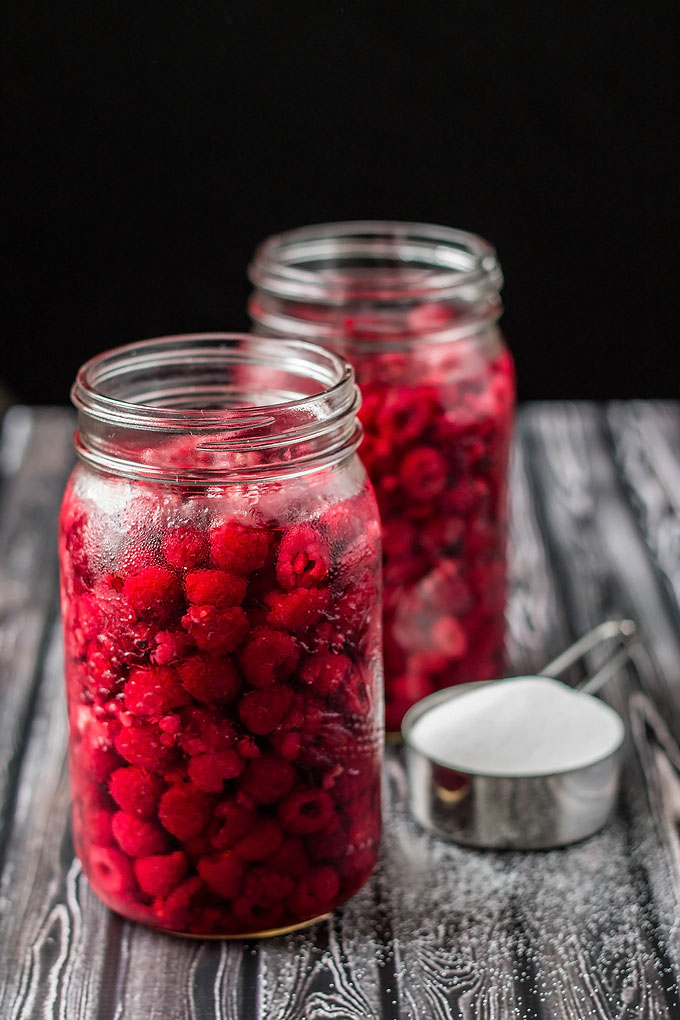 two mason jars full of raspberries, sugar and vodka
