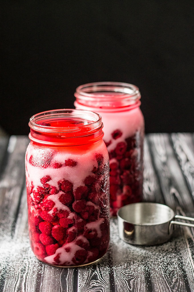 two mason jars full of raspberries, sugar and vodka to make raspberry vodka